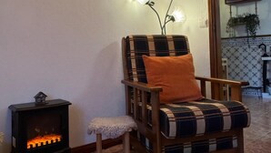 Ett mysigt vardagsrum med ett träpanelat tak, en mönstrad fåtölj med en orange kudde, en liten värmare och en väggmonterad lampa.