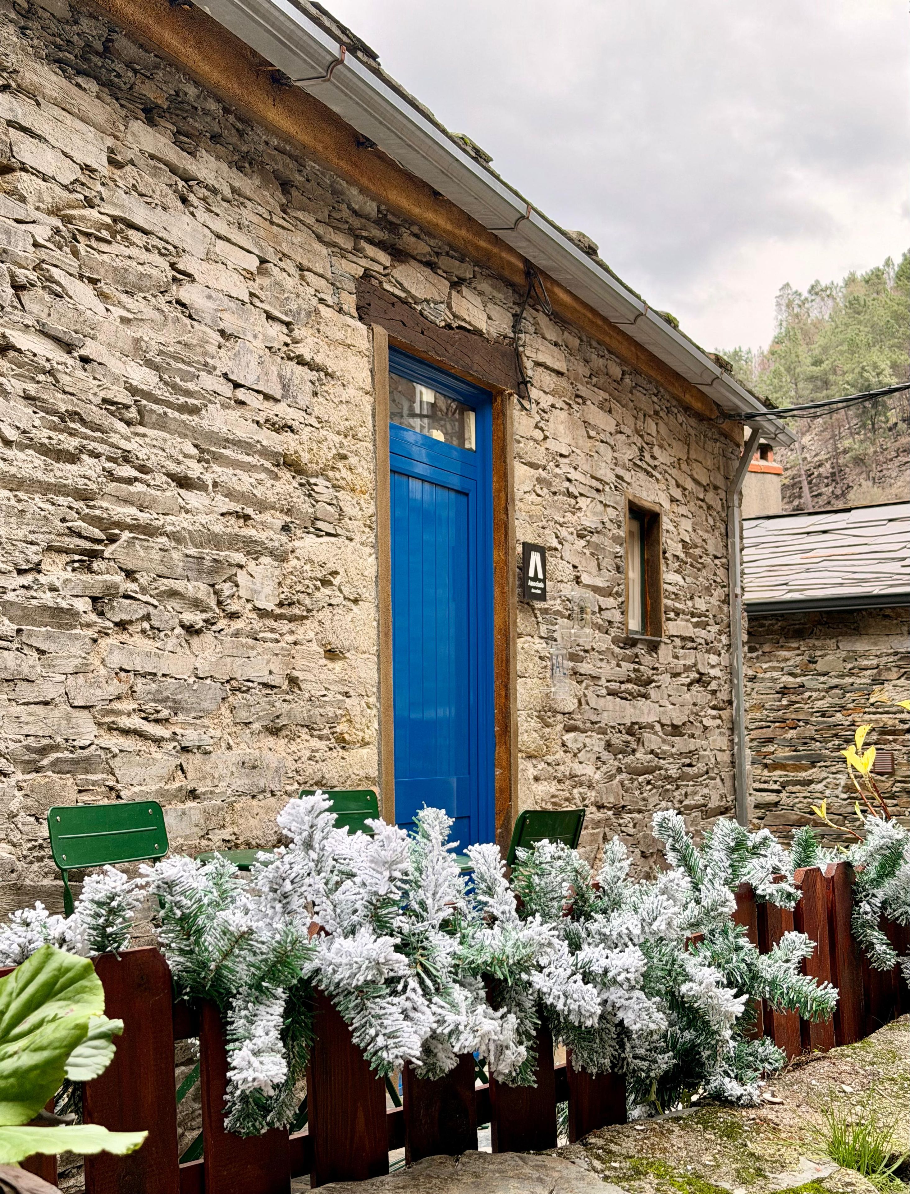 Un edificio de piedra con una puerta azul, una ventana pequeña y un letrero.
