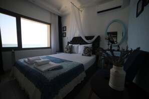 A bedroom with a large bed, a bedside table with a vase, a window with curtains, and a mirror on the wall.