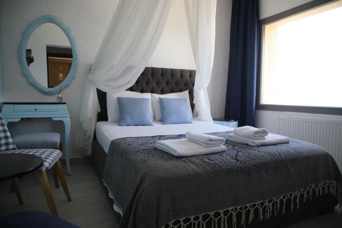 Quarto com cama, cadeira, penteadeira, espelho e janela com cortinas.