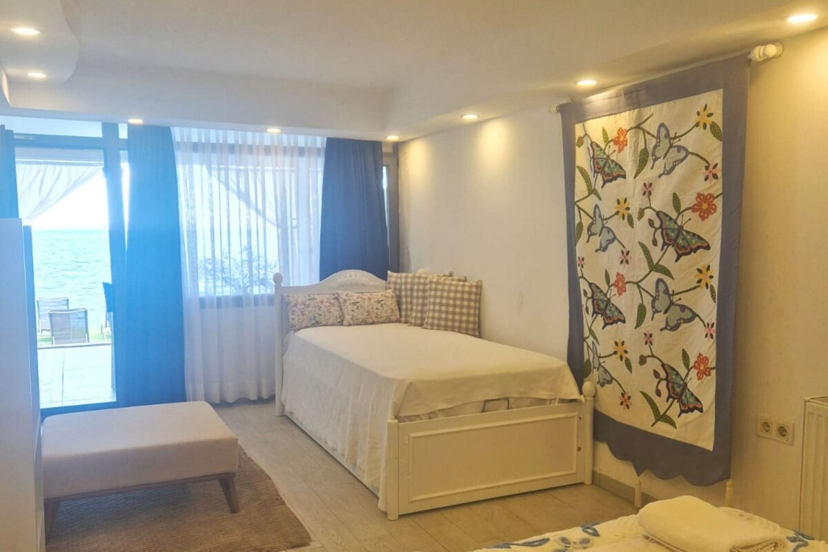 A bedroom with a bed, a bench, a window with curtains, and a radiator.