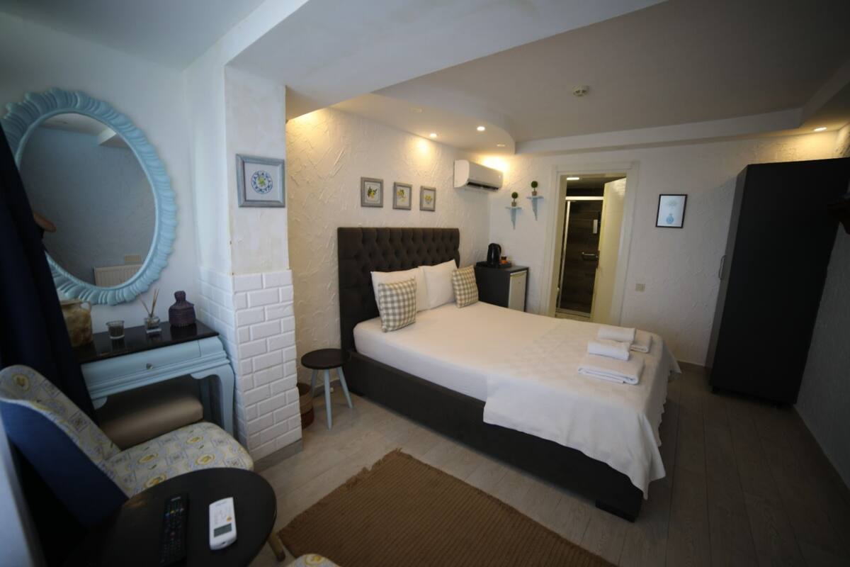 Um quarto com uma cama grande, uma cômoda, uma cadeira, um espelho e uma mesinha de cabeceira com um controle remoto.