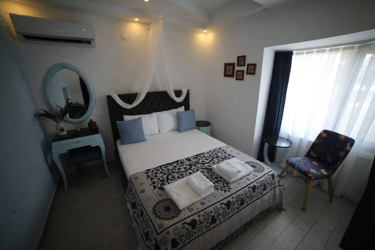 Quarto com cama, mesa de cabeceira, cadeira e janela com cortinas.