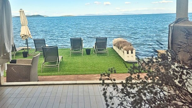 Eine Terrasse mit Meerblick, ausgestattet mit vier Liegestühlen, einer kleinen Gartenanlage und einer Pergola.