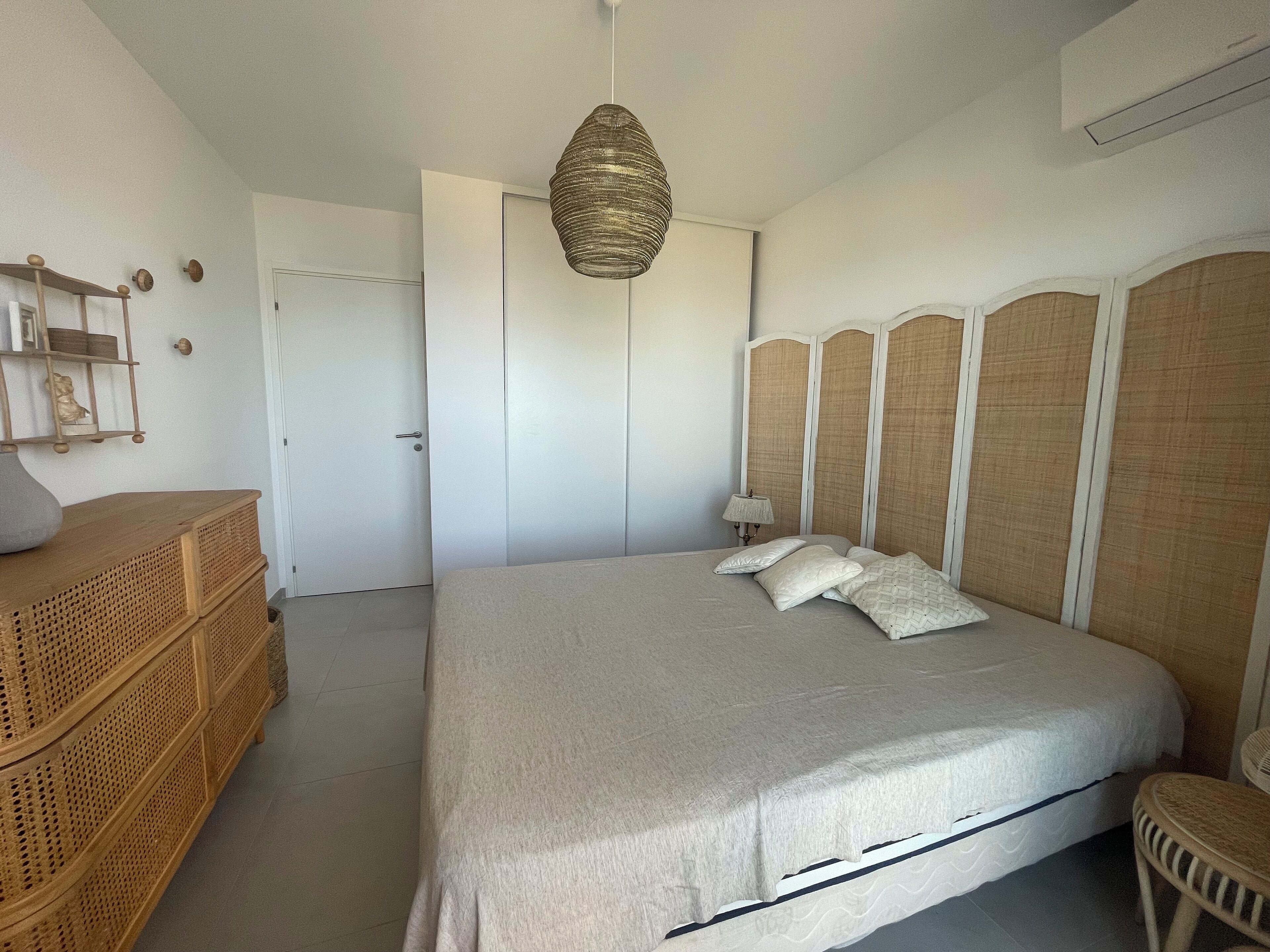 A bedroom with a bed, a bedside table, a lamp, a wardrobe, and a hanging light fixture.