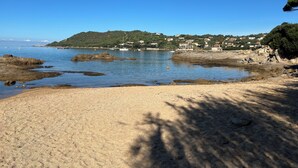 Ein Strand mit felsigem Ufer, klarem blauen Wasser und einer Hügelside mit Gebäuden.