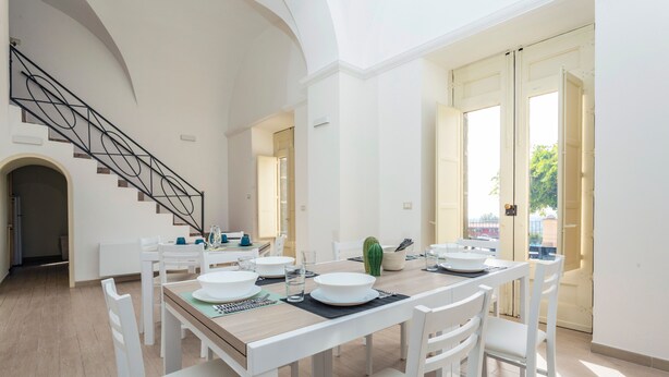 A dining area with a wooden table, white chairs, and a staircase. - Badimà Villa with Pool (Aci Sant'Antonio)
