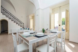 Un espace repas avec une table en bois, des chaises blanches et un escalier.