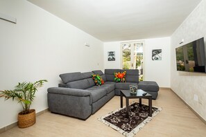 A modern living room with a grey sectional sofa, a small table, a potted plant, and a TV mounted on the wall. - Badimà Villa with Pool (Aci Sant'Antonio)