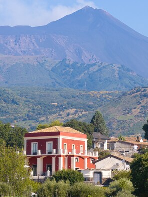 Un bâtiment rouge doté de balcons, entouré de verdure et avec une montagne en arrière-plan.
