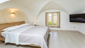 A bedroom with a bed, a TV, a window with a view, and a curved ceiling. - Badimà Villa with Pool (Aci Sant'Antonio)