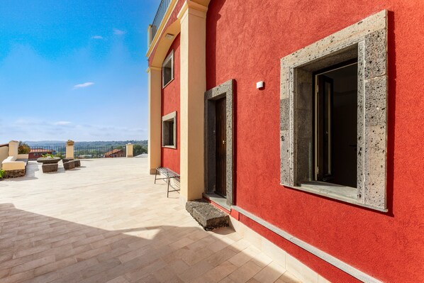 A red building with a balcony, a bench, and a view of the landscape.
