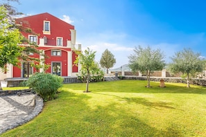 A red building with a stone pathway, a grassy lawn, and trees. - Badimà Villa with Pool (Aci Sant'Antonio)