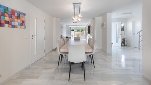 A modern dining area with a long table, chairs, and a chandelier.