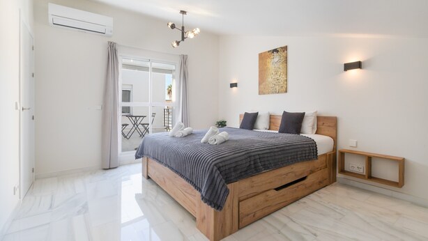 A bedroom with a wooden bed, a balcony, a ceiling light, and a wall-mounted light fixture.