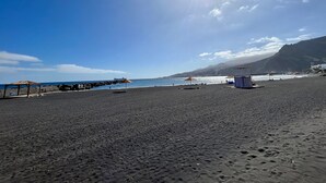 Una playa con sombrillas, una torre de salvavidas y un litoral rocoso.