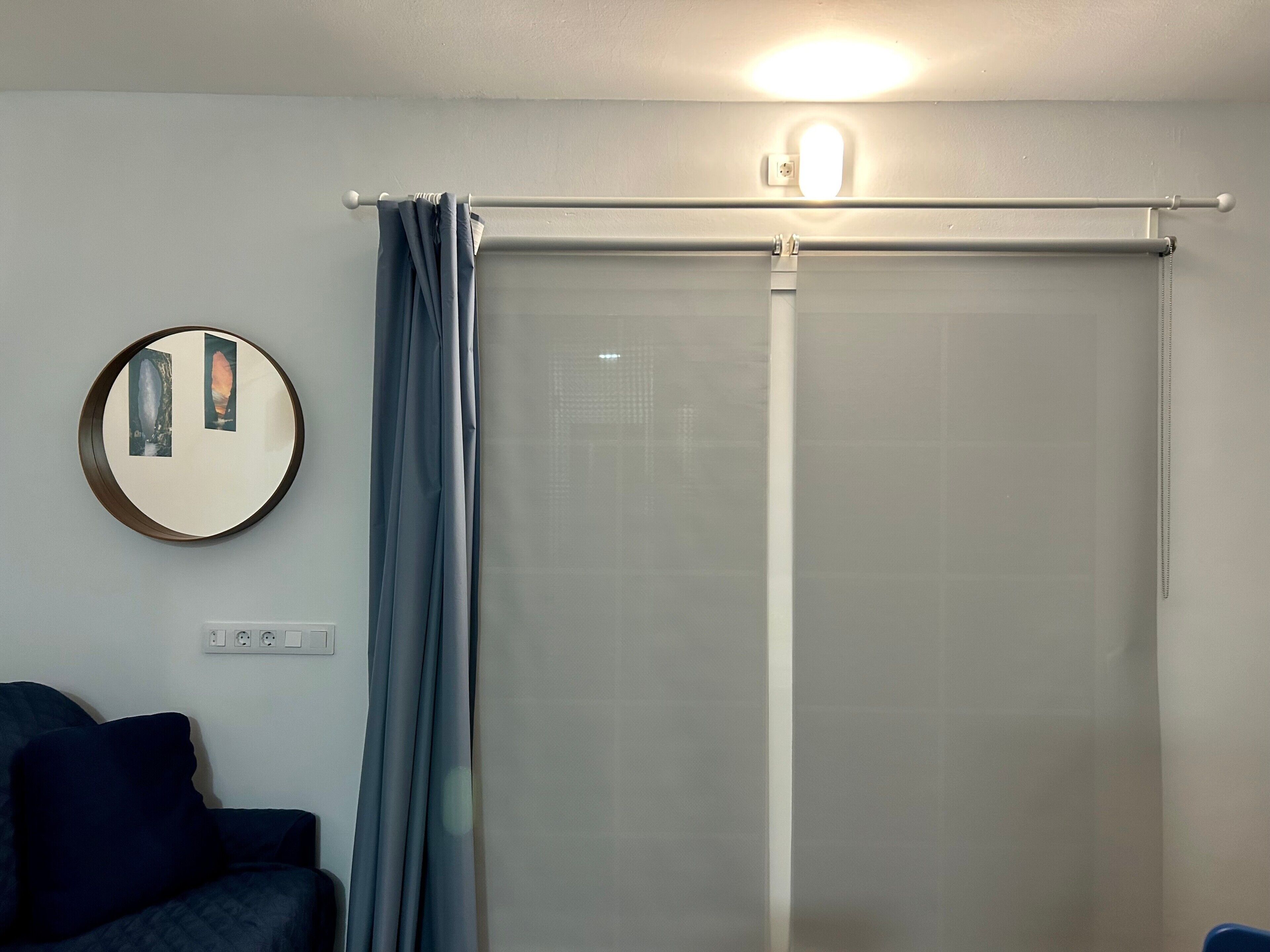 Een kamer met een bed, een ronde spiegel, een gordijn en een lamp.
