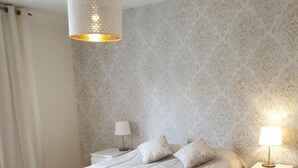 A bedroom with a bed, two bedside tables, a hanging light fixture, and a patterned wall. - Apartment 'Fernandes' with Mountain View, Wi-Fi and Air Conditioning (Carvoeiro)