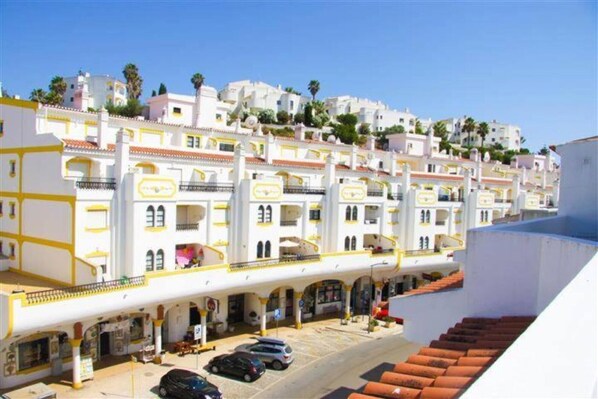 A row of white buildings with yellow accents, a covered walkway, and parked cars.