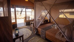 A room with a bed, a table, and a chair. There is a window with a view of the outside. - Africa Safari Serengeti Kusini  (Bariadi)