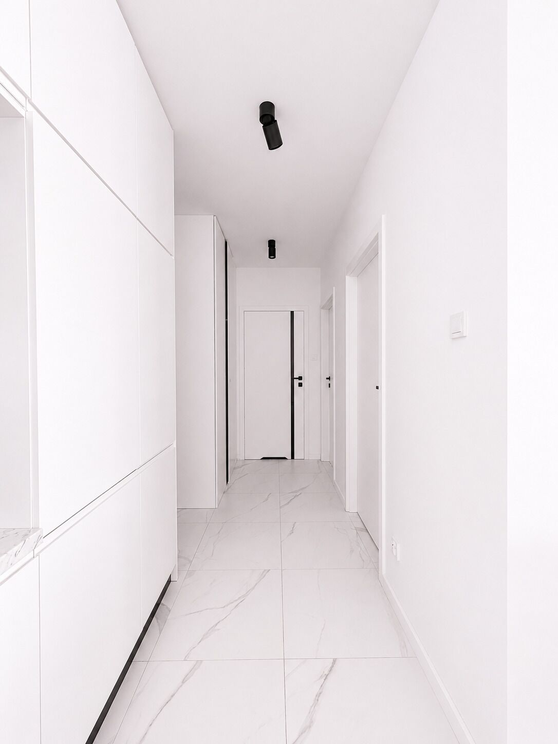 Un pasillo con paredes blancas, piso de baldosas y una puerta al final.