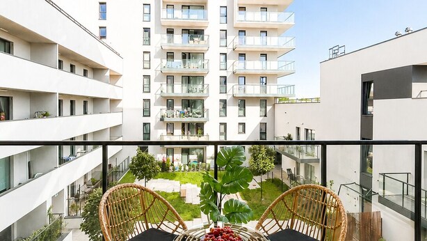A balcony with two wicker chairs and a glass table, overlooking a residential building complex. - Lumina 3-room apart on Drewnowska (Lódz)