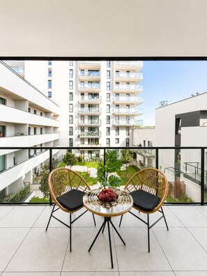 A balcony with two wicker chairs and a glass table, overlooking a residential building complex. - Lumina 3-room apart on Drewnowska (Lódz)