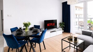 A modern living room with a dining area, a flat-screen TV, and a sofa. - Lumina 3-room apart on Drewnowska (Lódz)