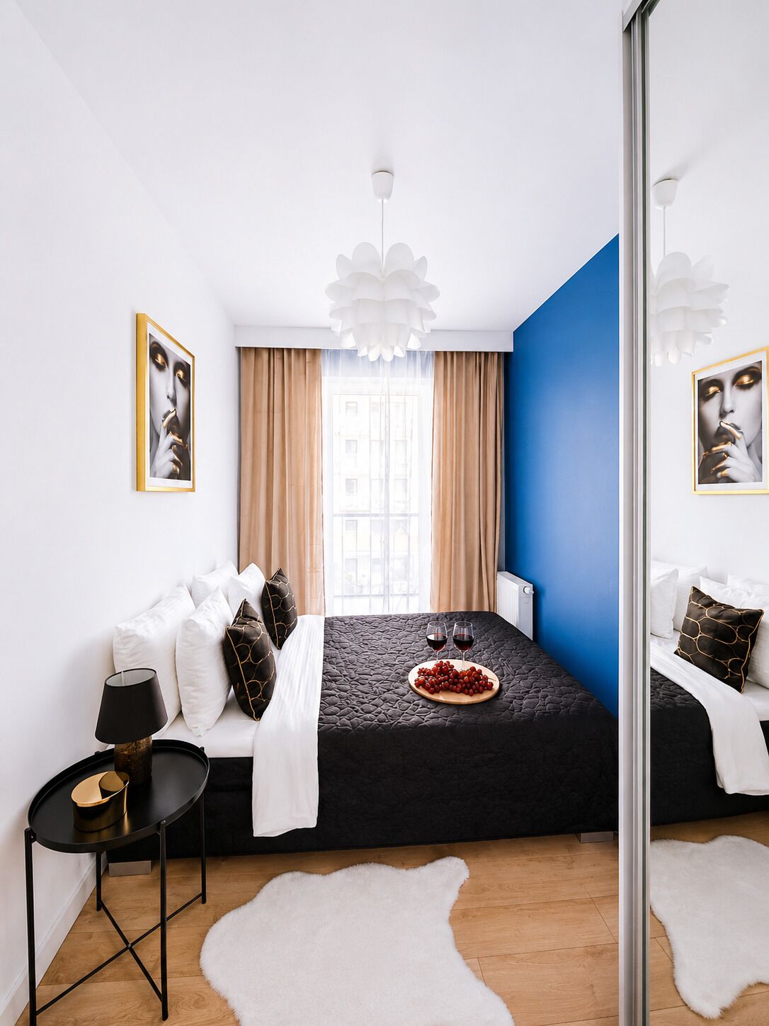 Een moderne slaapkamer met een bed, een klein tafeltje, een spiegel en een raam met gordijnen.