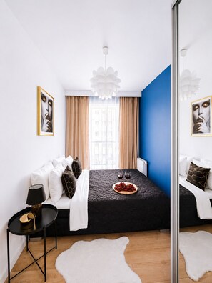 A modern bedroom with a bed, a small table, a mirror, and a window with curtains. - Lumina 3-room apart on Drewnowska (Lódz)