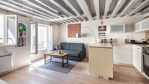 A modern apartment with exposed ceilings, a grey sofa, a small kitchen, and artwork on the walls.