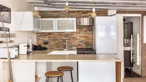 A modern kitchen with a brick backsplash, white cabinetry, and a central island with stools.