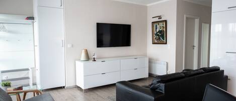 A modern living room with a white sofa, a black sofa, a dining table, and a TV mounted on the wall.