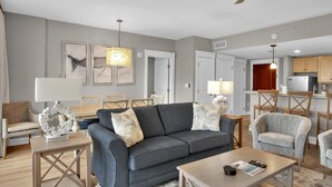 A modern living room with a grey sofa, wooden coffee table, and a dining area with a chandelier.