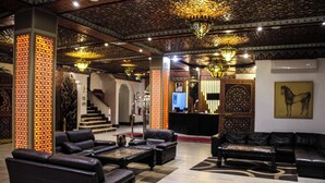 A lobby with leather sofas, a reception desk, and ornate ceiling decorations. - HOTEL LA PERLE DU SUD (Ouarzazate)