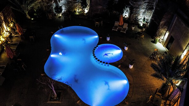 An aerial view of a pool area with a large, illuminated blue pool, surrounded by lounge chairs and tables. - HOTEL LA PERLE DU SUD (Ouarzazate)
