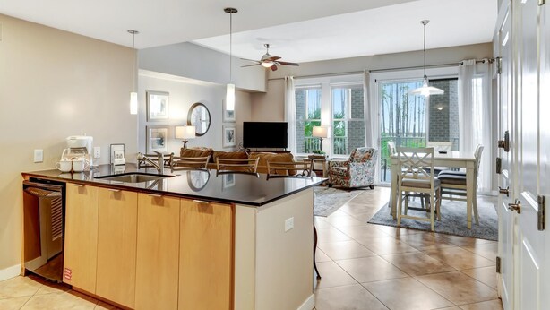 A modern kitchen with a central island, dining area with a table and chairs, and a view of the outdoors through large windows.