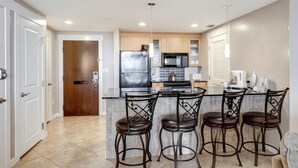 A modern kitchen with a central island, bar stools, and a microwave.