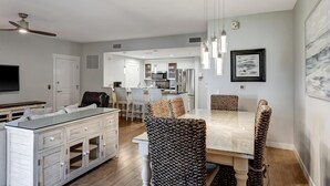 Une cuisine moderne dotée d’un îlot central, d’un coin repas avec des chaises en osier et d’un ventilateur de plafond.