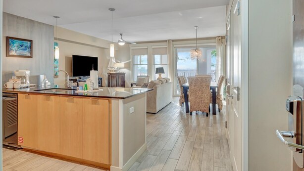 A modern kitchen with a central island, a dining area with wicker chairs, and a large window providing natural light. - Tranquil 3rd Floor Retreat: 2 Bedroom, 3 Bath, and two King Beds at Sandestin Golf and Beach Resort! (Miramar Beach)