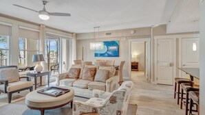A spacious living room with a large sofa, a coffee table, and a ceiling fan. There is a painting on the wall and a door leading to another room. - Tranquil 3rd Floor Retreat: 2 Bedroom, 3 Bath, and two King Beds at Sandestin Golf and Beach Resort! (Miramar Beach)