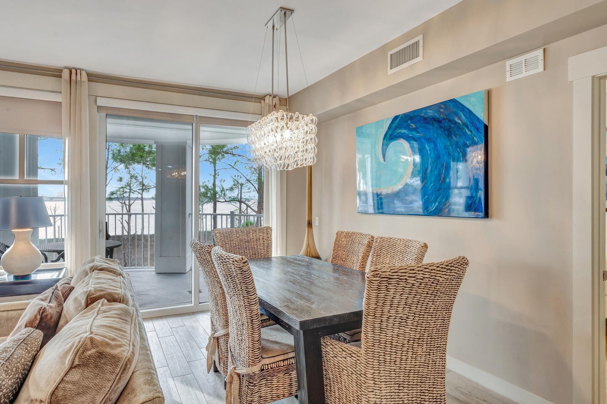 A dining area with a dark wooden table and wicker chairs, a chandelier, and a large abstract painting on the wall.