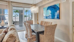 A dining area with a dark wooden table and wicker chairs, a chandelier, and a large abstract painting on the wall. - Tranquil 3rd Floor Retreat: 2 Bedroom, 3 Bath, and two King Beds at Sandestin Golf and Beach Resort! (Miramar Beach)