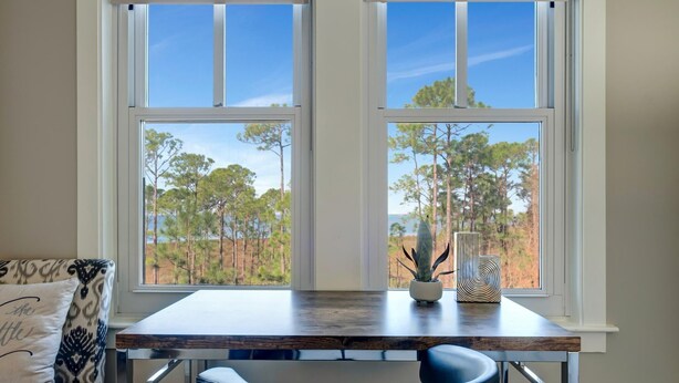 A room with a wooden desk and chair, a window with a view of trees, and a patterned pillow on a couch. - 3rd-Floor Bayfront Serenity: 2 Bedroom, 3 Baths, Sunset Views, Private Balcony at Sandestin Golf and Beach Resort! (Miramar Beach)