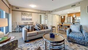 A spacious living room with a sofa, armchairs, a coffee table, and a dining area with a table and chairs. There is a kitchen area with a refrigerator and a sink. - 3rd-Floor Bayfront Serenity: 2 Bedroom, 3 Baths, Sunset Views, Private Balcony at Sandestin Golf and Beach Resort! (Miramar Beach)