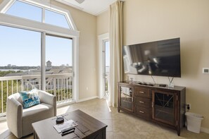 Ein Balkon mit Blick auf die Stadt, ein großer Flachbildfernseher, eine Holzkommode und ein weißer Mülleimer.