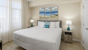 Ein Hotelzimmer mit einem großen Bett, zwei Nachttischen mit Lampen, einem Strandkissen und einem Gemälde mit einer Strandansicht.