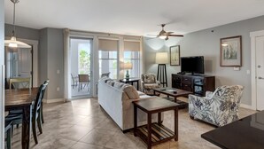 A spacious living room with a sofa, two armchairs, a coffee table, a TV, and a dining area with a table and chairs.