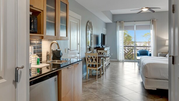 A compact hotel room with a kitchenette, a balcony with a view, and a bed.