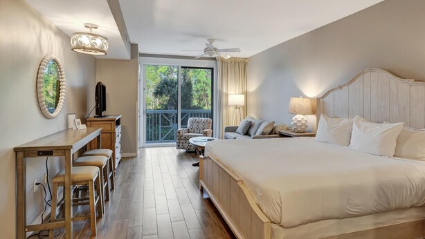 Habitación de hotel con una cama grande, un escritorio con una silla, una mesita y un balcón con una silla.